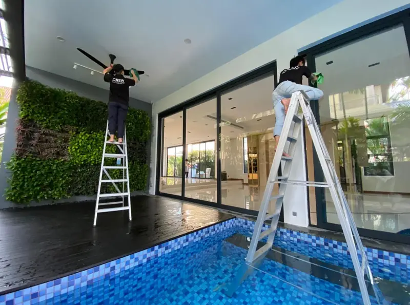 OCD cleaners on ladders cleaning high glass beside a pool